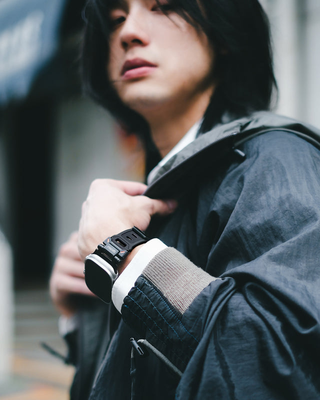 A man with long hair and a jacket posing to show his Apple watch strap and case