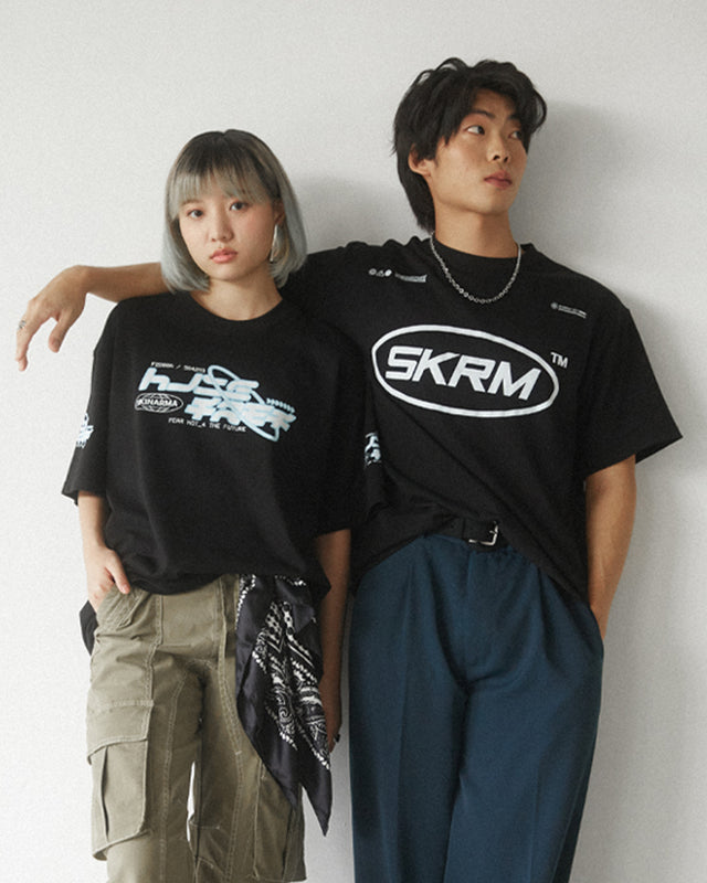 A young man and woman wearing Skinarma shirts, standing side by side